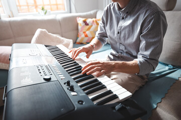 Close-up of hands playing a digital keyboard under warm natural light, capturing the essence of...
