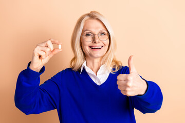 Confident mature businesswoman in blue pullover giving thumbs up on beige background