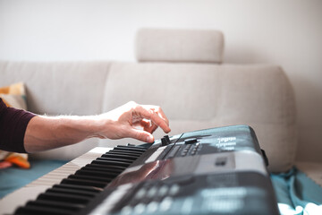Close-up of a digital keyboard with a hand playing a melody, illuminated by soft natural light. The...