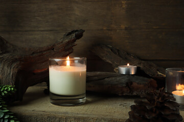 burning luxury aromatic scented candle glass on wooden table with background of vintage wooden wall...