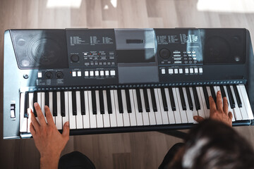 Man playing a digital keyboard in a relaxed home setting, seated on a sofa with natural light...