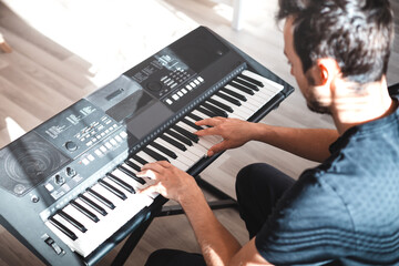 Man playing a digital keyboard in a relaxed home setting, seated on a sofa with natural light...