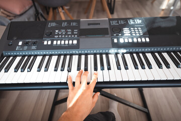 Close-up of a digital keyboard with a hand playing a melody, illuminated by soft natural light. The detailed controls and keys evoke creativity and musical exploration