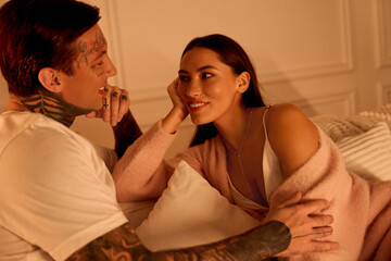 Two people enjoy an intimate conversation while relaxing on a bed, sharing smiles and affection.