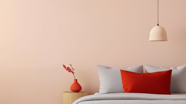 A cozy bedroom featuring a light pink wall, a soft gray bed, red accent pillows, and a decorative vase with flowers.