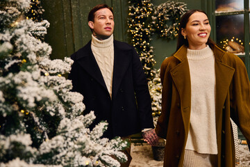 A young couple walks hand in hand through a snowy landscape, embracing the festive spirit.