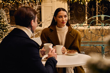 A loving couple shares warm beverages and pastries while seated outside in a festive atmosphere.