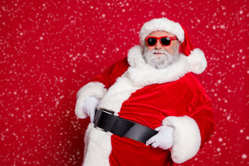 Photo of funny fat santa claus wear red headwear hat dark glasses smiling empty space celebrating noel isolated red color background