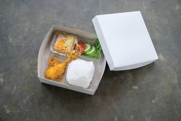 Serving boxed rice in a white cardboard box or paper box. White rice, chili sauce, cucumber, vegetables, fried chicken.