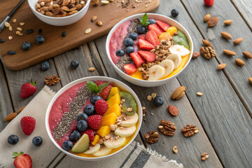 Colorful smoothie bowls with fresh fruits, nuts, and seeds on a rustic wooden table - Powered by Adobe