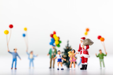 Miniature Santa Claus holding a gift surrounded by children and colorful balloons