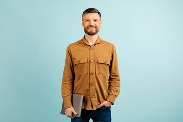 middle aged smiling modern male teacher holding laptop, isolated on gray background. High quality photo