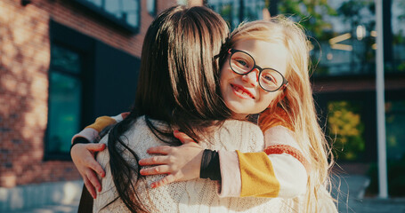 Camera focus on cute Caucasian girl hugging her mother. Child looking at camera while smiling with...