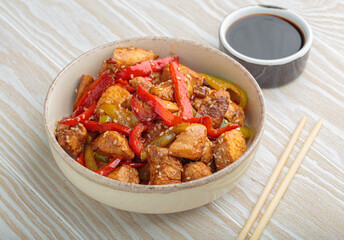 Chicken stir fry with red and green bell peppers sprinkled with sesame seeds, served in bowl, with chopsticks and soy sauce aside, composing a delicious asian meal