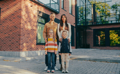 Front view of Caucasian family standing together. Looking at camera while smiling. Little brother and sister posing for best shot in front of mother and father. Kids ready for first day at school.