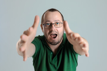 Naklejka premium Cheerful man reaching both hands toward the camera with a friendly smile, creating a welcoming and engaging vibe. Shot on a neutral gray background, emphasizing positivity and connection