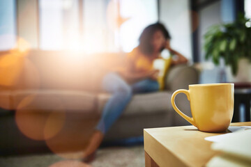 Blur, coffee on table and cup for wellness with woman on sofa in living room of home to relax....