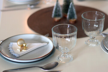 Table set for Christmas meal with plates, glasses, holiday decorations, lit candles and wine. Selective focus.