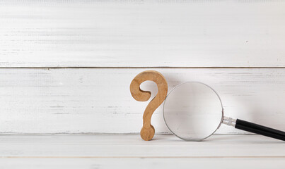 Wooden Question Mark with Magnifying Glass on White Wooden Background Symbolizing Research and Inquiry