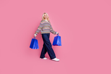 Full body portrait of nice aged woman mall bags walk empty space wear sweater isolated on pink color background