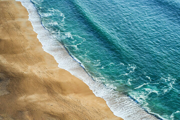 A breathtaking aerial view of a sandy beach and crystalclear ocean waters from a majestic cliff...