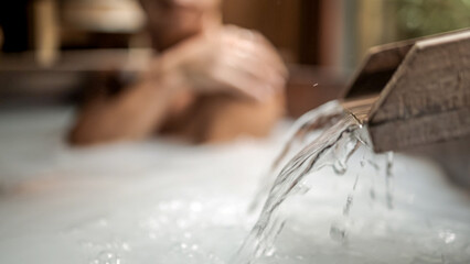 A young woman relaxes in a powdery Japanese bath in a tropical setting. Selective focus on flowing water. A serene spa experience. Spa and wellness concept.