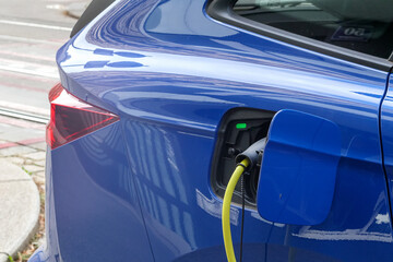 A blue electric car is parked at a charging station on the road