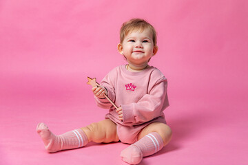 Cute newborn baby girl in a pink princess bodysuit sitting on a pink background, holding magic wand...
