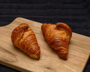 Two freshly baked croissants sit on a wooden board, highlighting their flaky layers and golden-brown crusts. The cozy kitchen setting adds warmth to this delightful treat
