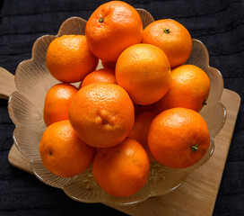 A bowl filled with vibrant clementines sits on a wooden surface. The bright fruit contrasts with the dark background, creating a visually appealing display perfect for a kitchen