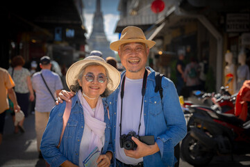 Fototapeta premium Asian retired couple happily hang out together in city full people city full buildings in capital Thailand Bangkok