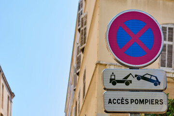 Street sign in Marseille, France, indicating no parking and firefighter access. The sign features a tow-away warning and is located on a historic street with old architecture.