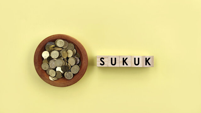 Top view coins in wooden bowl with SUKUK words on yellow background. Islamic shariah financing concept