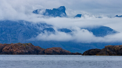 Overcast Summer Day. Panoramic view of islets in the fjord with high mountains shrouded in clouds in the background. Lofoten Islands, Northern Norway.