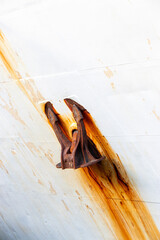 A rusted ship anchor mounted on a weathered, white metal hull, with streaks of rust cascading down,...