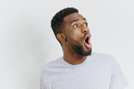 Surprised young african american man with wide open mouth expressing shock and amazement against a white background