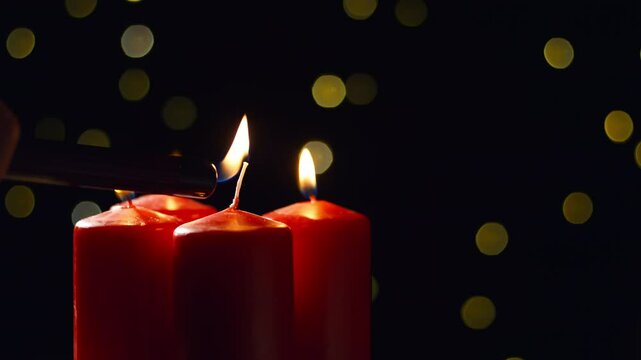 Hand lighting the fourth red Advent candle on a festive background, close up shot. Christmas celebration, hope, peace, joy, and love concepts.