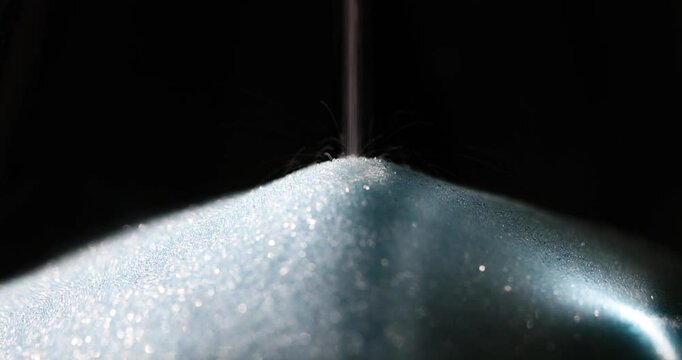 Flow of sparkling sugar grains creating pile against black. Crystal structure of sweet product catches light gently glowing in dark