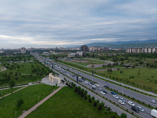 Naklejka premium City landscape. Evening view from a drone of the city before sunset and mountains on background. Trees, roads, streets, cars and buildings in summer. Beautiful clouds on the blue sky. Vivid scenery.