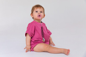 Cute baby girl in a pink bodysuit sitting on a white background and looking up at empty copy space. Closeup. Childhood and fashion. Birthday party concept. High quality photo