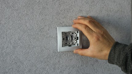 male hand applying white plastic switch housing to base in wall with gray wallpaper, DIY home...
