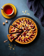 Plum pie on a marble cutting board with cup of tea. Grey background. Top view.