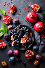 Fruits assortment, pomegranates, grapes, figs, plums on black plate. Dark background. Top view.