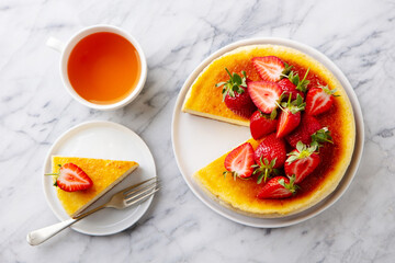 Cheesecake dessert with fresh strawberries and cup of tea. Marble background. Close up. Top view.