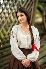 Fototapeta premium Beautiful brunette braided girl in rural long Ukrainian dress working on nature. Pretty young model in countryside art photo. 