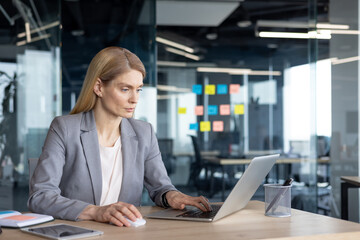 Mature woman businesswoman in modern office focused on laptop, working on project planning and collaboration with professionalism. Reflects business leadership, diligence and efficiency.