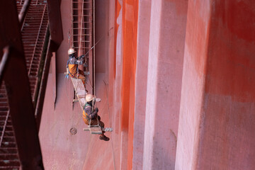 crew members painting cargo hold using fallen chair hanging from hold inspection platform