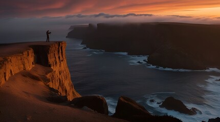 A lone photographer stands on a cliff edge, capturing a breathtaking sunset over rugged sea cliffs. The scene conveys adventure, solitude, and the beauty of nature at dusk.