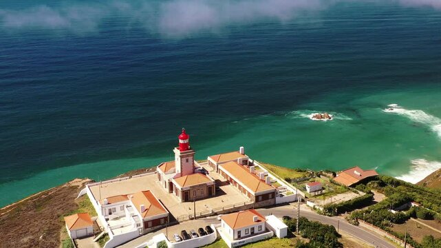 Dramatic drone footage of Cabo da Roca Lighthouse and monument, revealing the stunning cliffs and ocean. Tourists explore this popular destination in Portugal, captured in a cinematic style