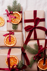 Wrapped gifts with dried orange and velvet pine branches and bows on white linen Christmas decoration diy recipe copy space flat lay top view holiday inspiration